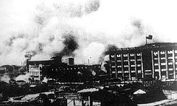 外国记者从上海公共租界建筑物中所拍摄的四行仓库保卫战中，在上海闸北四行仓库顶楼随风飘荡的中华民国国旗。（公有领域）